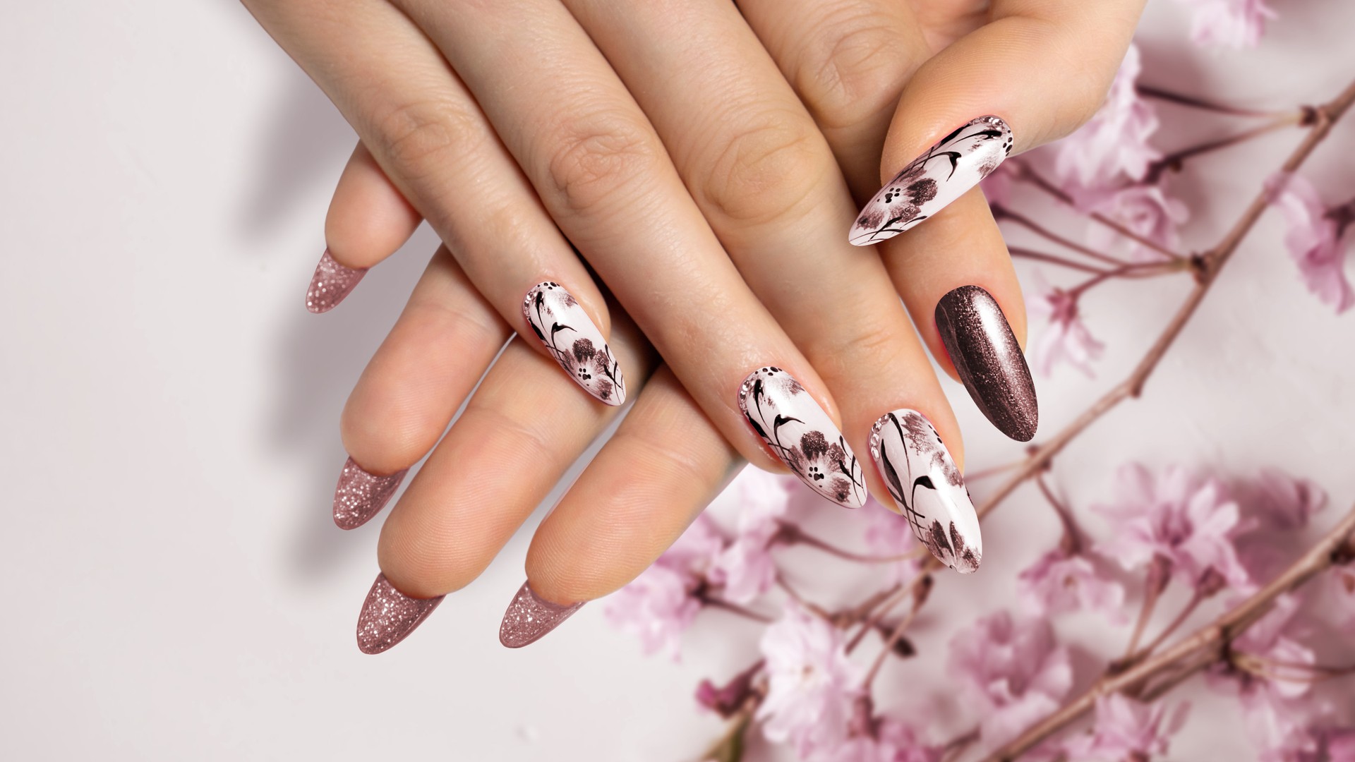 Close-up of a brown manicure on long, sharp nails on a flower background with a painted flower design.
