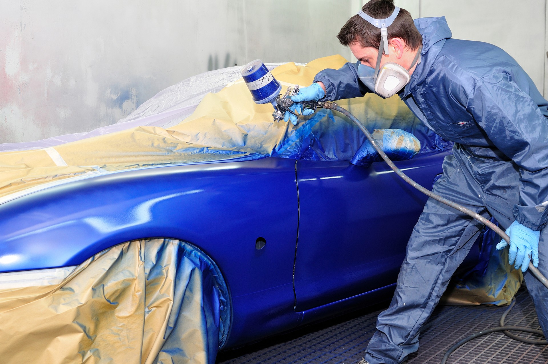 Male worker painting exterior of a blue car against wall